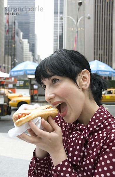 Junge Frau beißt auf der Straße stehend in ein Hotdog  New York City
