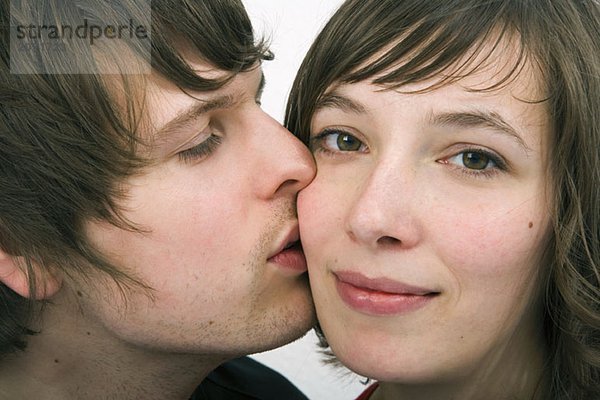Ein junger Mann küsst eine junge Frau auf die Wange