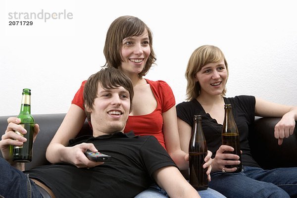 Drei junge Erwachsene sitzen auf dem Sofa und trinken Bier