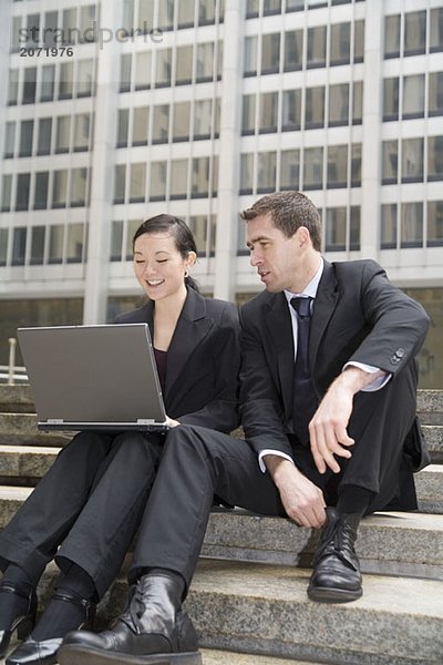 Ein Geschäftsmann und eine Geschäftsfrau mit Laptop auf den Treppen vor einem Bürohaus