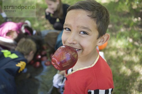 Ein kleiner Junge mit einem Apfel im Mund während weitere Kinder im Hintergrund Äpfel aus einer Wanne fischen