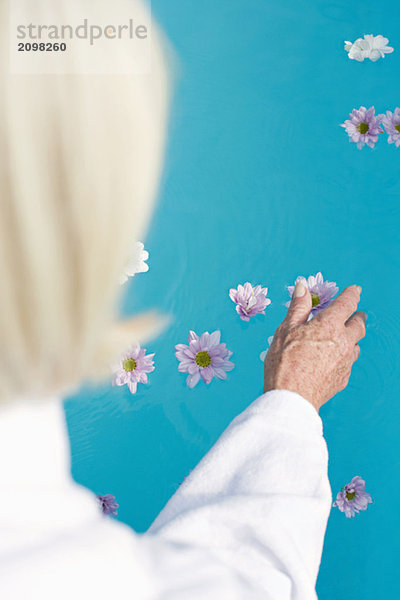 Deutschland  Seniorenfrau beim Berühren von Blumen auf der Wasseroberfläche