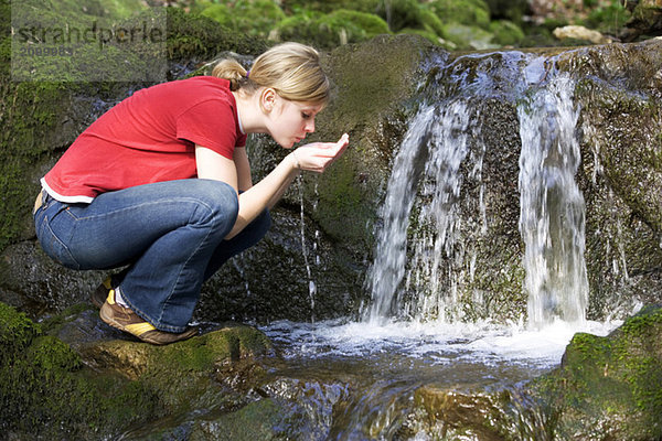 Junge Frau trinkt Wasser aus dem Bach  Seitenansicht