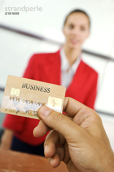 Menschliche Hand hält Kreditkarte mit Geschäftsfrau im Hintergrund  Nahaufnahme
