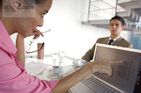 Geschäftsfrau beim Einchecken des Laptops mit Geschäftsmann im Hintergrund