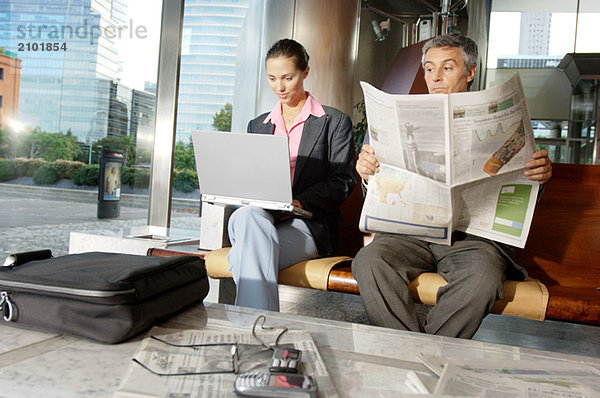 Geschäftsfrau mit Laptop während Geschäftsmann Zeitung liest