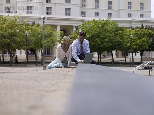 Geschäftsfrau und Businessman sitting in der Nähe von Brunnen mit laptop