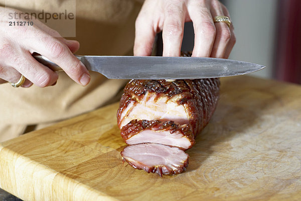Oven roasted ham being sliced on cutting board with large knife