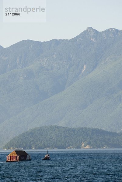 Tug Boat pulling logs through the ocean with mountains in the background  Howe Sound  BC