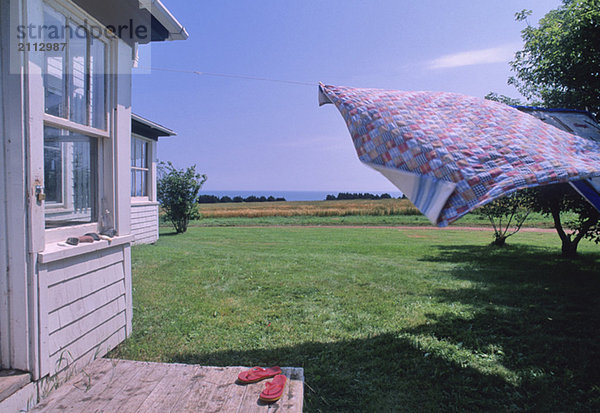 Handmade Quilt blowing on laundry line  farmhouse and ocean visible  PEI