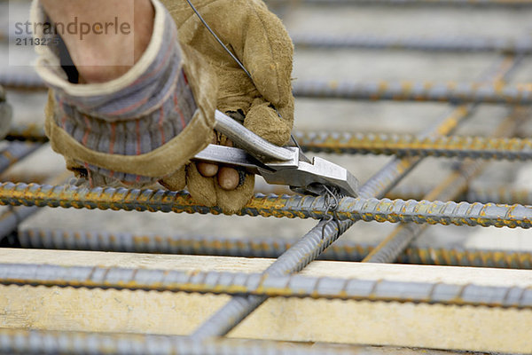 'Workers gloved hands tying rebar with pliers and metal wire