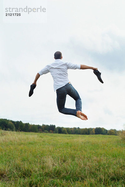 Barfuß springender Mann auf einem Feld