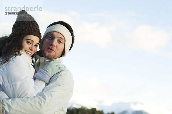 Junges Paar in Winterkleidung  umarmend  lächelnd vor der Kamera
