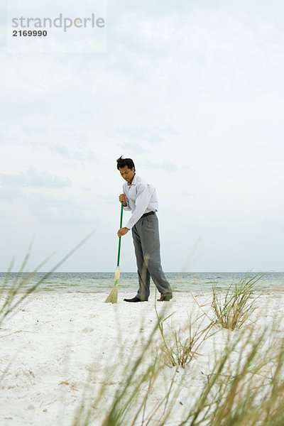 Mann steht am Strand und fegt Sand mit Besen