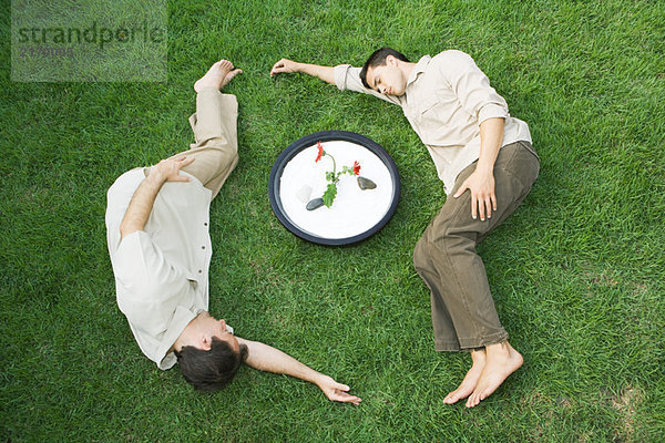Zwei Männer liegen auf Gras um Schale mit Blume  Augen geschlossen