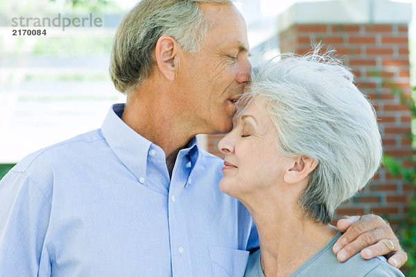 Reifer Mann  der die Stirn seiner Frau küsst  Seitenansicht