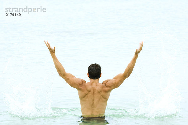 Muskulöser Mann im Schwimmbad stehend mit erhobenen Armen  Rückansicht
