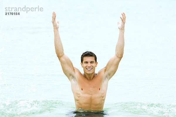 Muskulöser Mann im Schwimmbad mit erhobenen Armen  lächelnd in die Kamera.