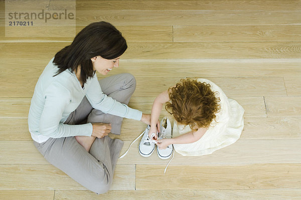 Mutter und kleines Mädchen sitzen auf dem Boden  Mädchen lernt Schnürsenkel zu binden  Blick von oben