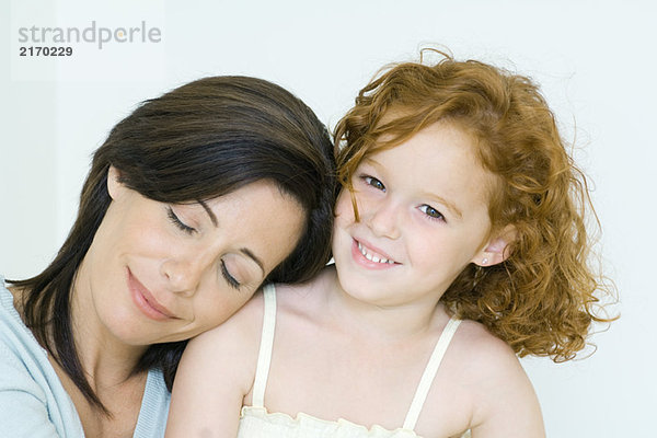 Mutter und Tochter  Frau ruht Kopf auf der Schulter des Mädchens  Mädchen lächelt vor der Kamera