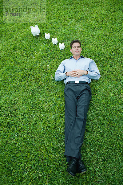 Mann auf Gras liegend mit geschlossenen Augen  Spardose neben dem Kopf