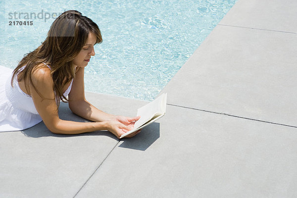 Frau auf dem Bauch neben dem Pool liegend  Lesebuch