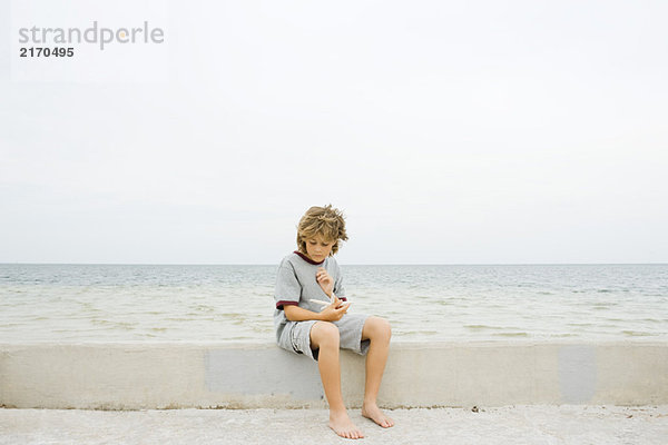 Junge sitzt auf einer niedrigen Wand am Strand und schaut auf den Seestern hinunter.
