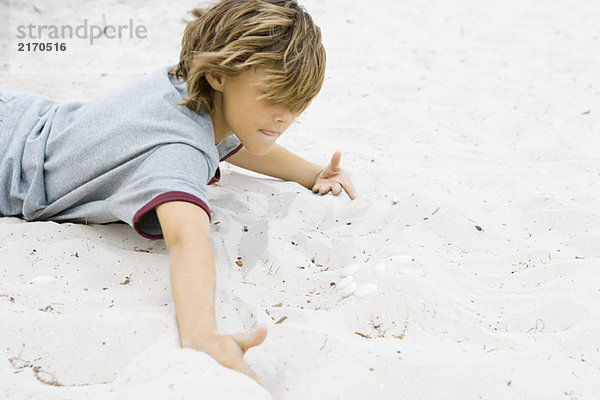 Junge auf dem Bauch liegend  im Sand grabend  Nahaufnahme
