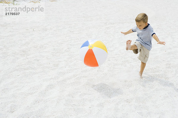 Kleiner Junge tritt Strandball am Strand  Arme ausstrecken
