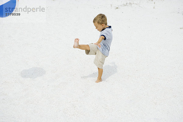 Kleiner Junge tritt Beachball am Strand  Seitenansicht