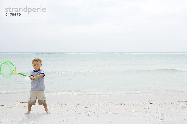 Kleiner Junge steht am Strand und hält das Netz hoch  um den Ball zu fangen.