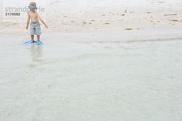 Junge mit Schwimmmaske und Flossen  knöcheltief im Wasser stehend