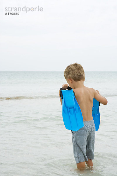 Junge steht knietief im Wasser  trägt Flossen  Rückansicht