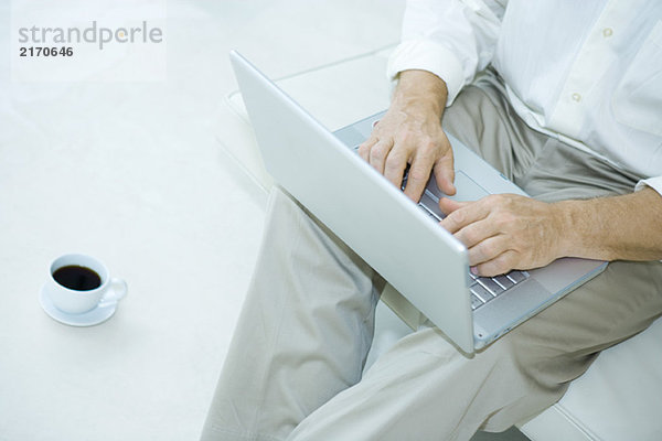 Mann sitzend mit Laptop  Tasse Kaffee neben ihm  Ausschnittansicht