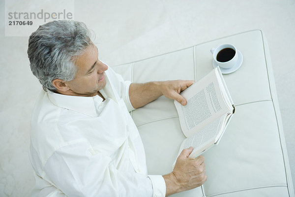 Erwachsener Mann neben Kaffeetasse liegend  Lesebuch  Hochwinkelansicht