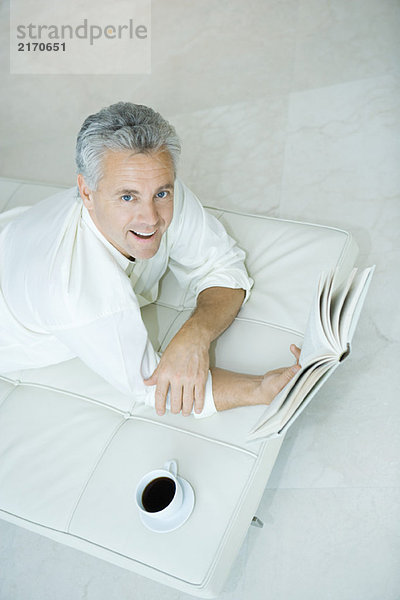 Erwachsener Mann auf Liegestuhl liegend  Buch haltend  Blick in die Kamera  hoher Blickwinkel