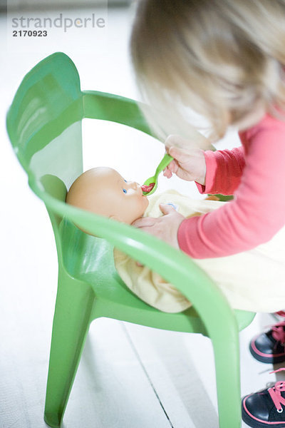 Blondes Kleinkind-Mädchen  das vorgibt  Babypuppe zu füttern.