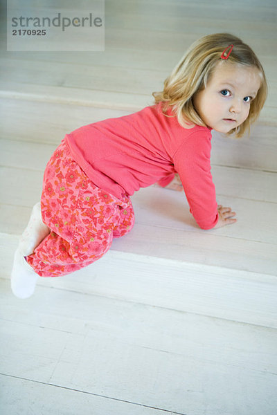 Blondes Kleinkind-Mädchen krabbelt auf Stufen  schaut über die Schulter in die Kamera
