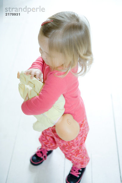 Blondes Kleinkind Mädchen hält Babypuppe verkehrt herum