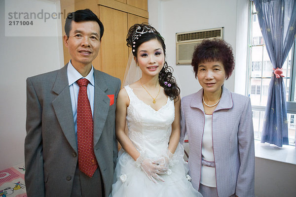 Braut steht zwischen den Eltern  lächelt in die Kamera  Porträt
