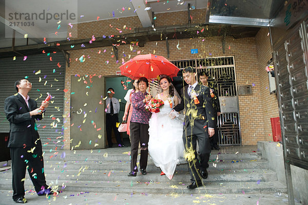 Chinesische Hochzeit  Braut und Bräutigam verlassen unter Konfetti  Braut mit rotem Sonnenschirm bedeckt