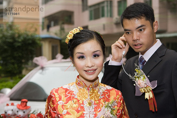 Braut in traditioneller chinesischer Kleidung  lächelnd vor der Kamera  Bräutigam hinter dem Kopfhörer