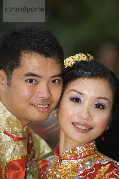 Frischvermählte in traditioneller chinesischer Kleidung  Wange an Wange  lächelnd vor der Kamera