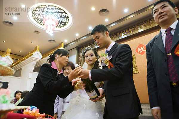 Frau hilft Braut und Bräutigam  Champagnerflasche öffnen  Blickwinkel niedrig