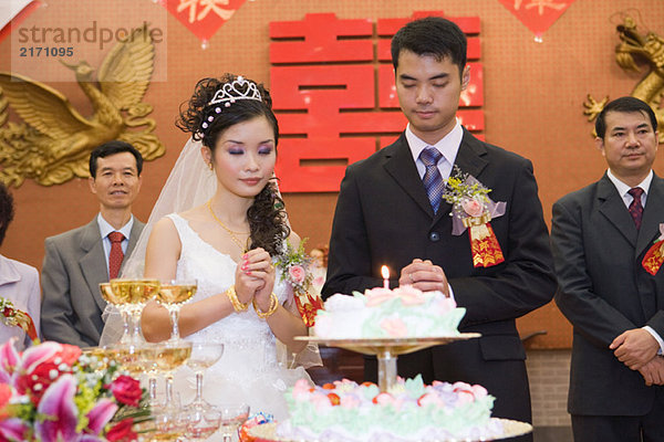 Frischvermählte stehen neben der Hochzeitstorte mit brennender Kerze  Augen geschlossen  gefaltete Hände