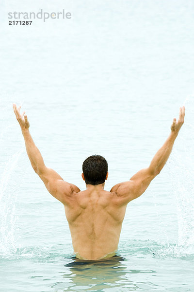 Muskulöser Mann hebt Arme aus dem Wasser  Rückansicht
