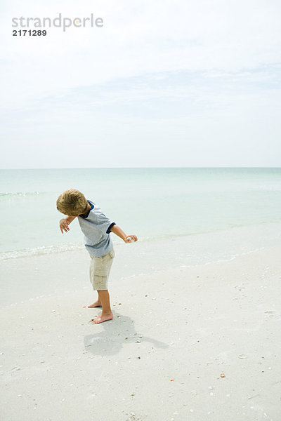 Junge am Strand wirft Felsen in Richtung Meer  volle Länge