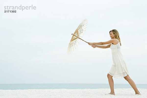 Frau hält Sonnenschirm am Strand  volle Länge