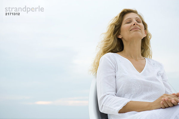 Frau sitzend mit geschlossenen Augen  lächelnd  Himmel im Hintergrund  Tiefblick