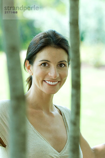 Frau lächelt Kamera durch Bäume  Porträt